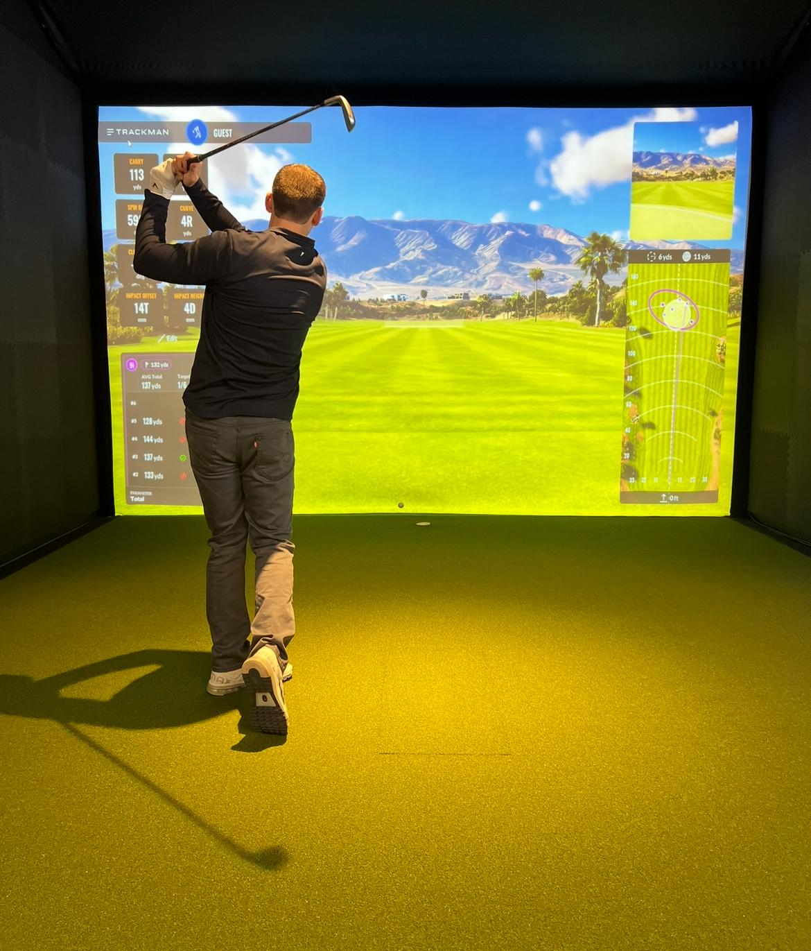 Indoor golf simulator bay with hitting mat and projection screen at Endless 18